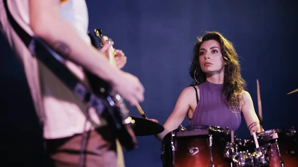 Pretty drummer playing on drums near blurred and tattooed guitarist — Photo de stock