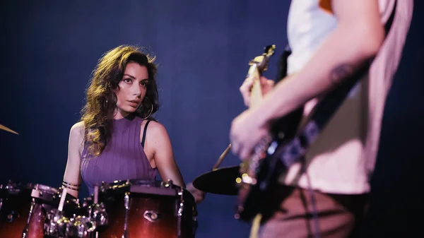 Pretty drummer playing on drums near blurred guitarist - foto de stock