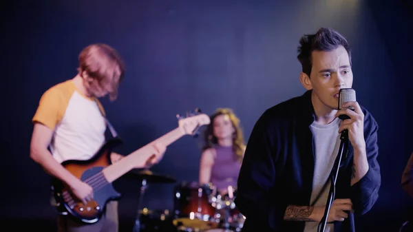 Tattooed young singer singing on stage with blurred music band — Photo de stock
