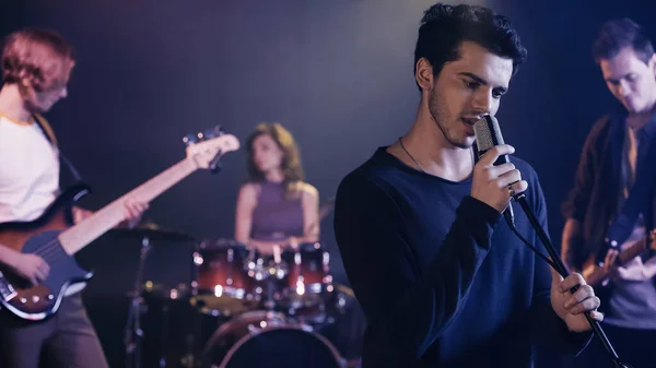 Young singer performing song with blurred music band — Stock Photo