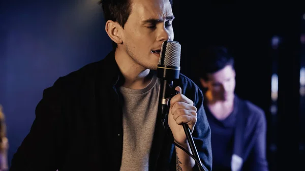 Tattooed man singing in microphone near blurred musician on stage — Photo de stock