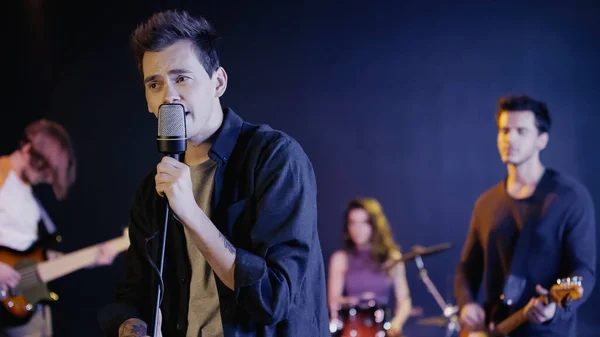 Young tattooed singer performing song with blurred music band — Photo de stock