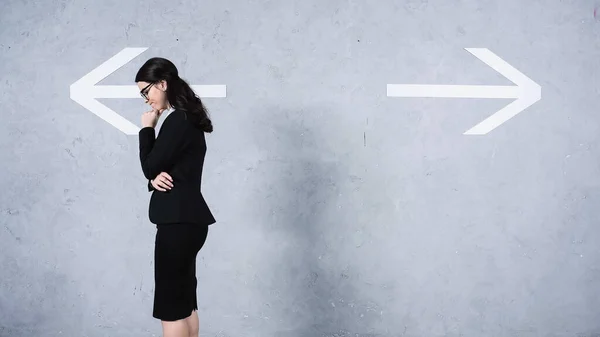Бізнес-леді в окулярах думаючи біля стріл на сірому — стокове фото