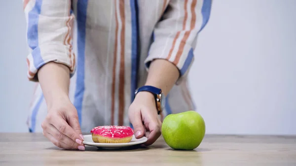 Cropped view of woman holding plate with doughnut near apple isolated on grey — стоковое фото