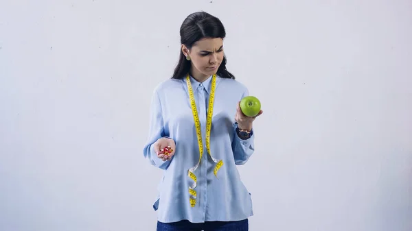 Brunette woman comparing vitamins and fresh apple isolated on grey — Stock Photo