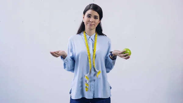 Mujer confundida comparando vitaminas y manzana aislada en gris - foto de stock