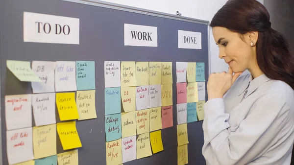 Pensive businesswoman thinking near sticky notes on board — Photo de stock