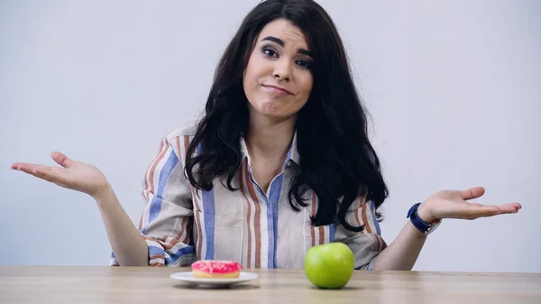 Woman showing shrug gesture near apple and doughnut isolated on grey — Fotografia de Stock