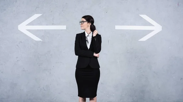 Businesswoman in glasses looking away near arrows on grey — Foto stock