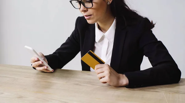 Morena empresaria sosteniendo teléfono inteligente y tarjeta de crédito aislado en blanco - foto de stock