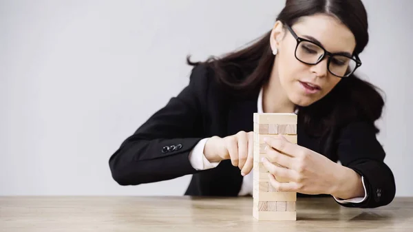 Brunette businesswoman playing blocks wood tower game isolated on grey — Stock Photo