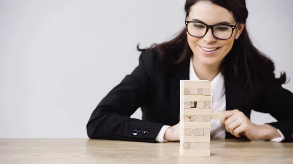 Cheerful businesswoman playing blocks wood tower game isolated on grey — стоковое фото