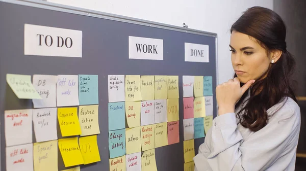 Pensive businesswoman thinking near colorful sticky notes on board — Stock Photo