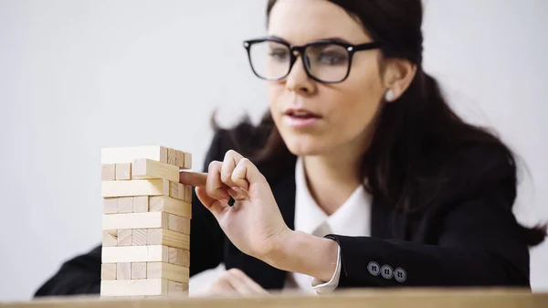 Blurred brunette businesswoman playing blocks wood tower game isolated on grey — стоковое фото