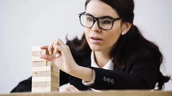 Blurred businesswoman in glasses playing blocks wood tower game isolated on grey — Stockfoto