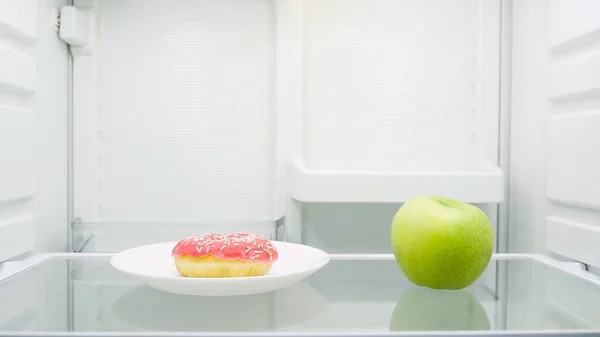 Sweet glazed doughnut on plate near green apple in fridge — Fotografia de Stock