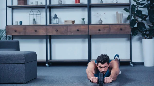 Bearded sportsman training with fitness wheel on floor at home — стоковое фото