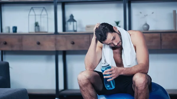 Deportista cansado con toalla sentado en la pelota de fitness y la celebración de la botella de deportes - foto de stock