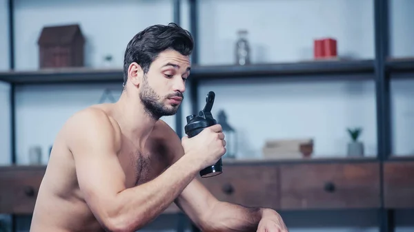 Muscular sportsman holding sports bottle at home — Stock Photo