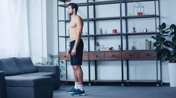 Comprimento total do homem muscular em shorts de pé perto do sofá — Fotografia de Stock