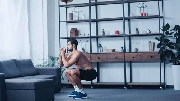 Full length of muscular man in shorts squatting near sofa — стоковое фото