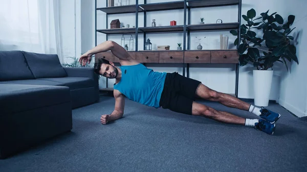 Young sportsman training in side plank pose at home — Fotografia de Stock