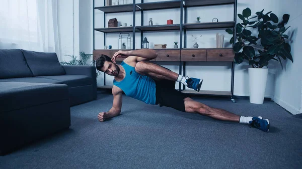 Muskulöser junger Sportler, der zu Hause in Seitenplanken-Pose trainiert — Stockfoto