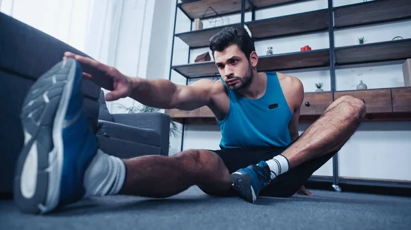 Muscular young sportsman stretching at home — Stock Photo