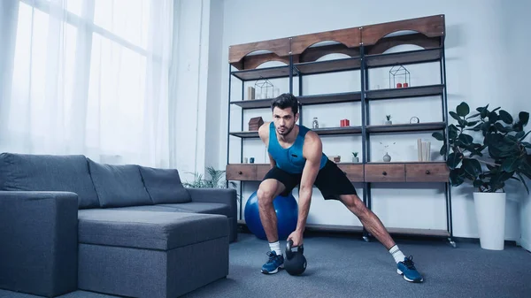 Muscular young sportsman in tank top weightlifting kettlebell — стоковое фото