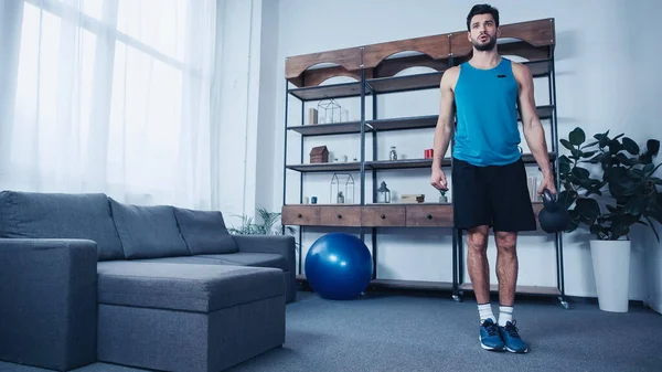 Bearded young sportsman in tank top weightlifting kettlebell — Stock Photo