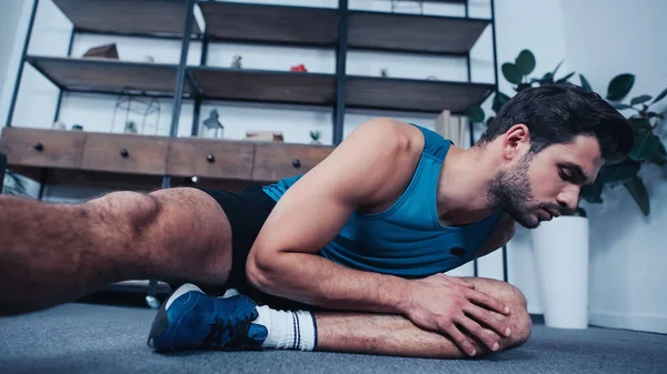 Young sportsman in tank top stretching at home — Stock Photo