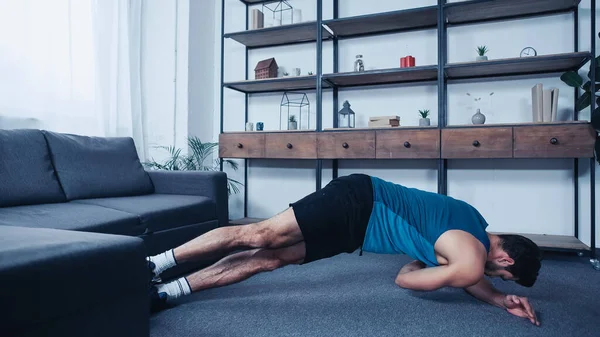 Young sportsman in tank top stretching on floor at home — стоковое фото