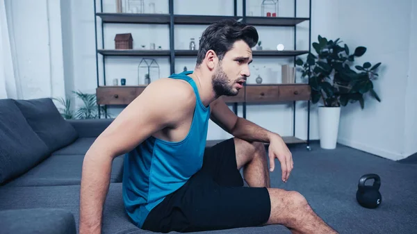 Müder Sportler im Tanktop neben verschwommener Kettlebell — Stockfoto