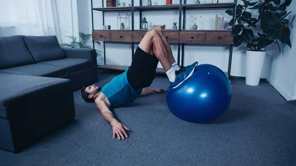 Bärtiger Sportler trainiert zu Hause auf blauem Fitnessball — Stockfoto