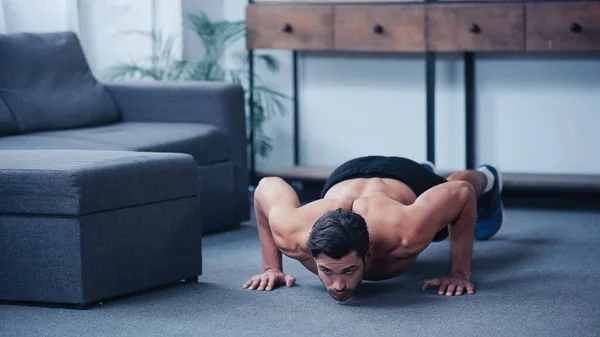 Vista a nivel de superficie del joven deportista haciendo flexiones de presión en el suelo en casa - foto de stock