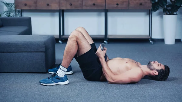 Deportista muscular haciendo ejercicio con kettlebell en el suelo en casa - foto de stock
