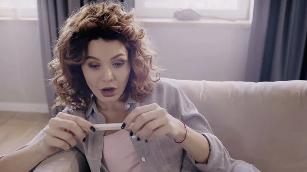 Mujer sorprendida mirando la prueba de embarazo en el sofá en casa — Stock Photo