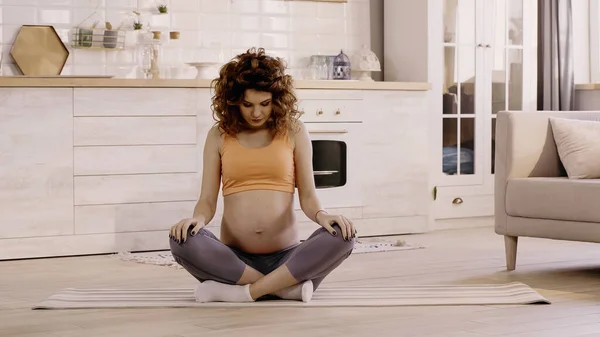 Pregnant sportswoman sitting on fitness mat at home — стоковое фото