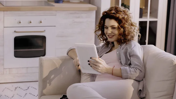 Щаслива вагітна жінка використовує цифровий планшет на дивані вдома — стокове фото