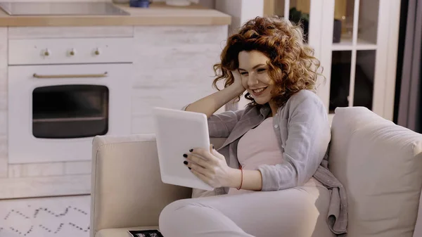 Веселая беременная женщина с помощью цифрового планшета возле ультразвукового сканирования ребенка на диване — стоковое фото