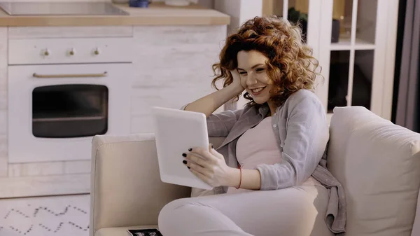 Cheerful pregnant woman using digital tablet near ultrasound scan of baby on couch — стоковое фото
