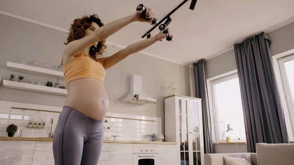 Low angle view of pregnant woman training with dumbbells at home — Foto stock