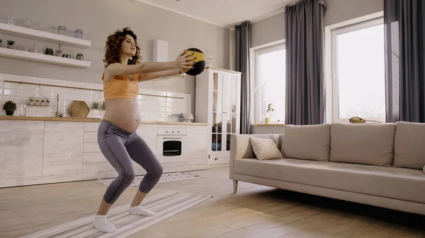 Беременная женщина тренируется с мячом дома — стоковое фото