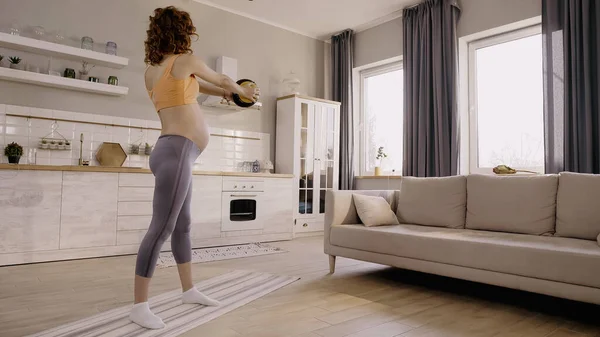 Pregnant woman working out with slam ball on fitness mat at home — Stock Photo