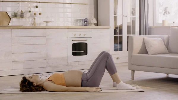 Side view of pregnant woman in sportswear lying on fitness mat at home — Foto stock