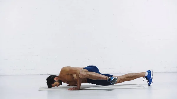 Sportif torse nu faisant de l'exercice sur un tapis de fitness près d'un mur de briques blanches — Photo de stock