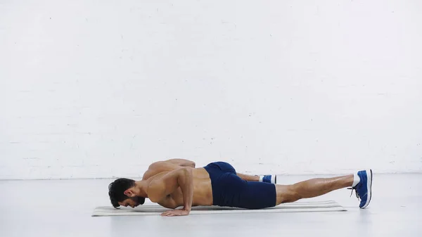 Sportif barbu faisant de l'exercice sur un tapis de fitness près d'un mur de briques blanches — Photo de stock