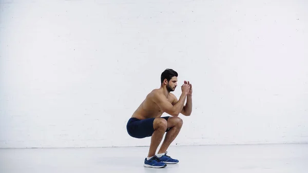 Junge Sportler in kurzen Hosen hocken in der Nähe einer weißen Ziegelwand — Stockfoto