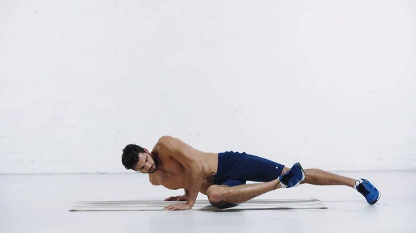 Comprimento total do desportista exercitando em uma postura de prancha de perna perto da parede de tijolo branco — Fotografia de Stock
