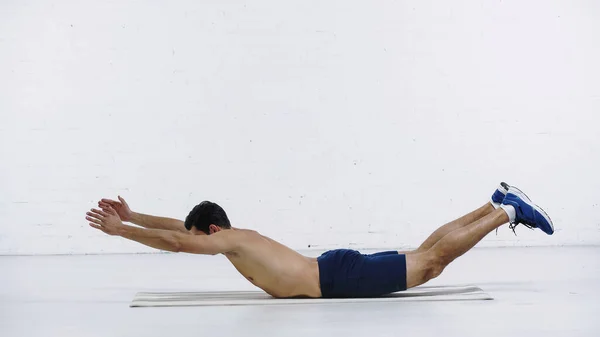 Full length of shirtless sportsman doing downward abs near white brick wall — Stock Photo